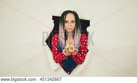 Woman With Toy House Looking Through Hole In Paper. Female With Afro Braids And Miniature Wooden Hou
