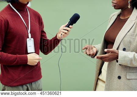 Medium Section Of Young Gallerist Holding Microphone Taking Interview Of African American Female Pho