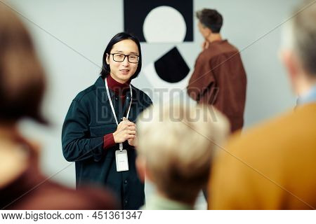 Young Asian Man Working In Modern Arts Gallery Standing In Front Of Group Of Unrecognizable People S
