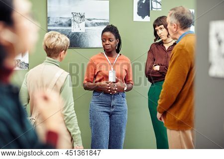 Portrait Of Young African American Gallery Worker Standing In Front Of Visitors Discussing Black And