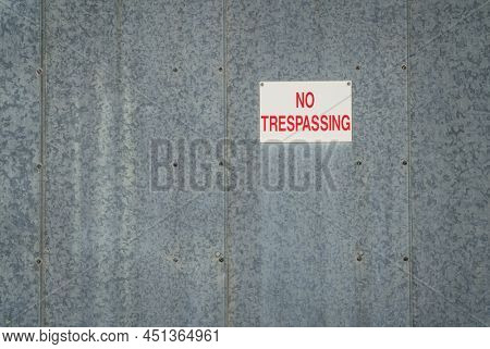 red and white no trespassing sign on a gavanized metal building wall