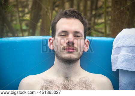Man Relaxing In An Outdoor Bath Surrounded By Trees, Around Camping Site In Gloucestershire, England
