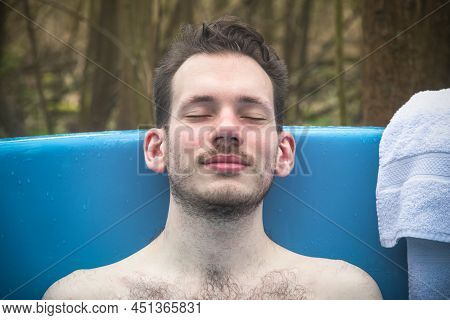Man Relaxing In An Outdoor Bath Surrounded By Trees, Around Camping Site In Gloucestershire, England