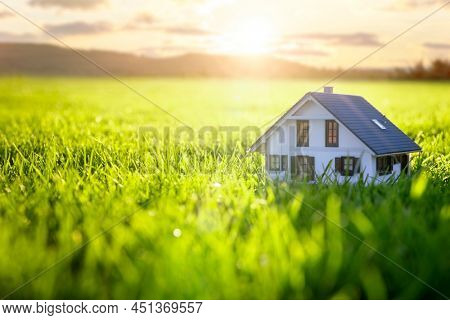 Model detatched house in empty green grass field at sunset background concept for construction and real estate