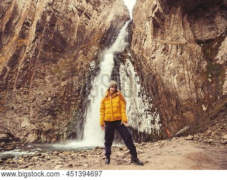 A Smiling Woman Stands Against The Backdrop Of An Icy Stormy Waterfall Flowing Down From Sheer Cliff