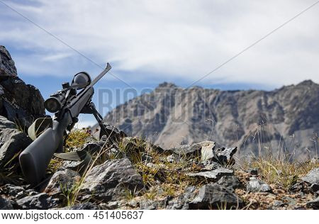 Sniper Rifle With Optical Sight On Bipods Among Rocks In The Mountains Against The Sky. High-precisi