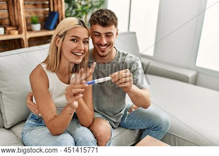 Young caucasian couple smiling happy holding pregnacy test at home.