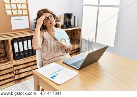 Middle age hispanic woman using handfan working at office