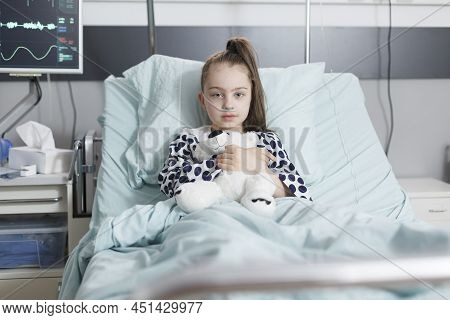 Ill Little Girl Holding Plush Teddybear And Wearing Oxygen Tube While Resting Alone In Hospital Bed.