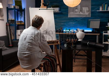 Senior Woman Feeling Inspired Looking At Creative Pencil Drawing Of Vase On Easel Sitting Down In Pr