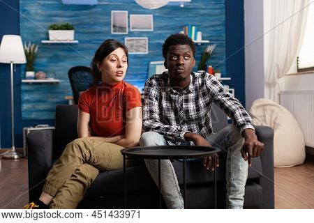 Irritated Young Multiethnic Couple Sitting On Couch In Living Room While Having An Argument And Marr