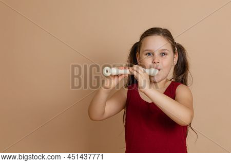 Girl In Red Dress Play Melody On Flute With Pleasure, Blowing Air Into Duct, Beige Background. Learn