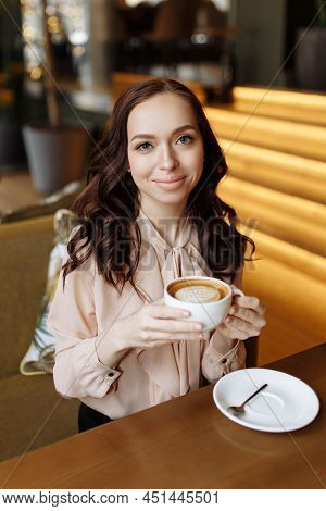 Beautiful Young Girl Drinks Coffee From A White Mug In A Cafe. Fragrant Drink With Beautiful Lattear