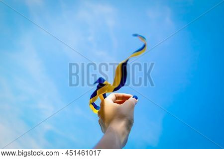 Hand Holds Blue Yellow Ribbon On Sky Background. Flag Of Ukraine Freedom Independence