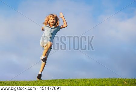 Little Adorable Boy Running On Grass. Excited Kid Play The Green Grass. The Child Has Blond Long Hai