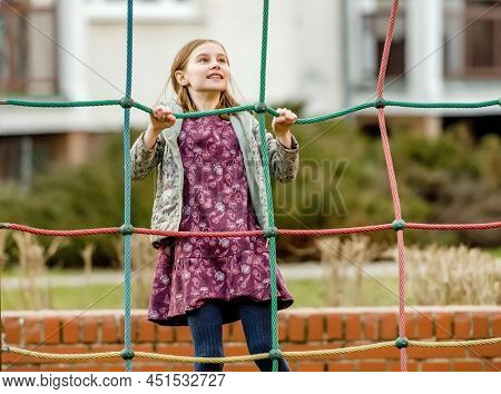 Preteen girl child playing outdoors and climbing at playgarden. Pretty kid enjoying walk