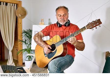 Mature Man Wearing Headphones Creating New Song While Playing Acoustic Guitar, Musical Keyboard Or S