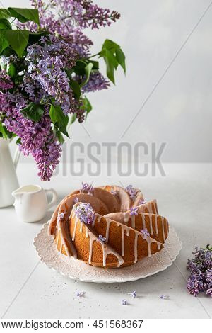 Vanilla Bundt Cake With Sugar Glaze And Lilac Flowers On White Background. Spring Composition. Homem