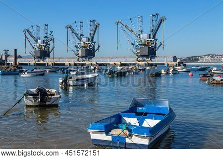 Trafaria; Portugal - March 01; 2022: Deep water terminal and silo for grain, derived products and oleaginous products in Trafaria, Portugal with fishing boats near the beach