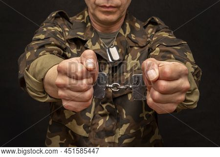 A military man in handcuffs holds an army badge in his hand on a dark background, selective focus 36