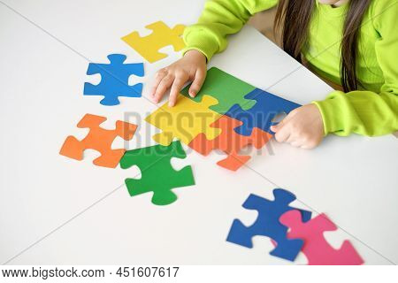 Child Collects A Puzzle Of Bright Multicolored Pieces While Sitting At A Table. International Symbol