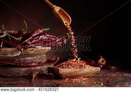 Chilli Flakes Are Poured Into A Wooden Dish. Chilli Flakes And Dried Chili Peppers On A Brown Backgr