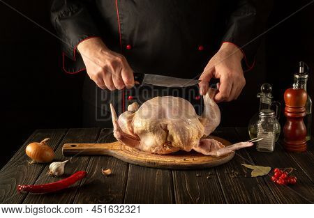 The Cook Cuts Raw Broiler Chicken With A Knife. Cooking A National Dish In The Restaurant Kitchen Wi