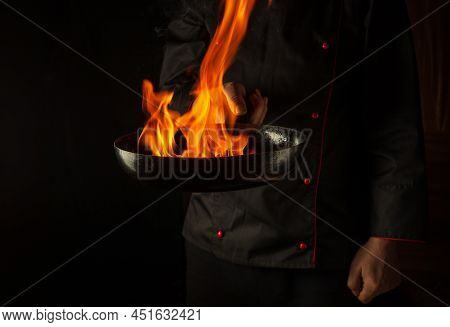 Cook Prepares Vegetable Food In A Frying Pan With A Flame Of Fire. The Concept Of Restaurant And Hot
