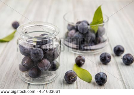 Top View Of The Small Sour Blue-black Sloes On A Glass Jar With Sloes On A Glass Bowl On A Grey Wood