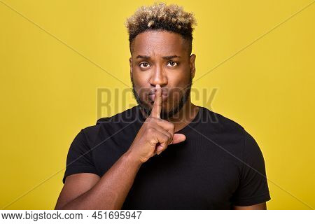 A Serious Black Man Put His Index Finger To His Mouth Calling For Silence, Against A Yellow Backgrou