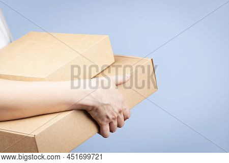 Stack Of Cardboard Boxes In Female Hands. Blank Brown Parcel Boxes On Light Blue Background. Packagi