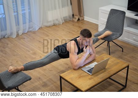 Flexible Man Work On Laptop And Doing Leg-split At Home. Concept Of Willpower, Motivation And Passio