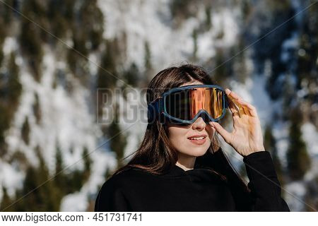 Portrait Of A Happy Girl In Ski Goggles On A Beautiful Background Of Mountains.