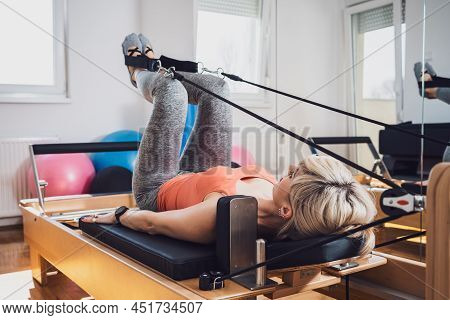 Woman Is Exercising On Pilates Reformer Bed In Her Home.