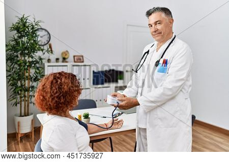 Middle age man and woman wearing doctor uniform using tensiometer having medical consultation at clinic