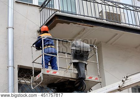 Worker In Hydraulic Lifting Ramp Repair The Balcony. Builder On Lifting Platform Standing Near The B