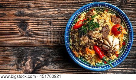 Traditional Uzbek Meal Called Pilaf. Rice With Meat On Plate With Oriental Ornament On A Dark Wooden