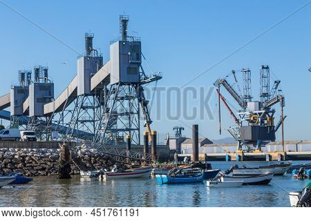 Trafaria; Portugal - March 01; 2022: Deep water terminal and silo for grain, derived products and oleaginous products in Trafaria, Portugal with fishing boats near the beach