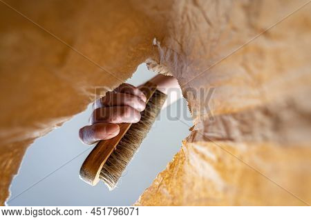 A Hand Places A Clothes Brush In A Paper Bag. A Mature Man's Hand Holds The Brush With A Wooden Hand