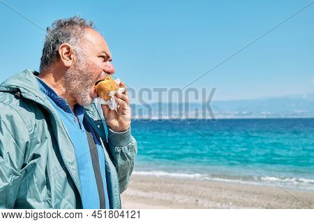 Bearded Mature Man At Spring Seaside Eating Hot Palatable Arancina (deep Fried Rice Balls With Meat)