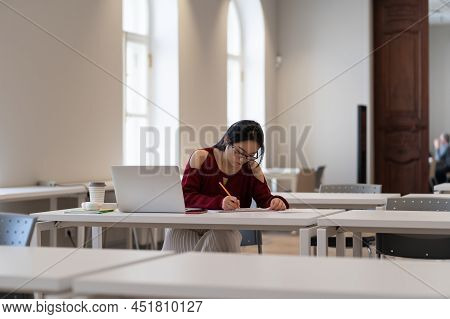 Focused Asian Student Prepare For Coursework In Library. Concentrated Girl Writing Speech For Gradua