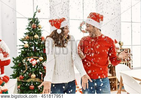 Young hispanic couple wearing christmas hat throwing conffeti celebrating new year at home.