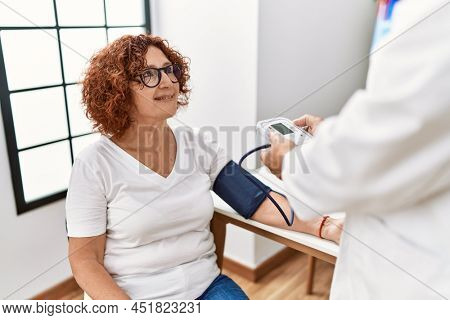 Middle age man and woman wearing doctor uniform using tensiometer having medical consultation at clinic