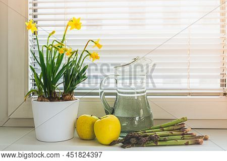 Spring Flowers Daffodils In Flower Pot, Fresh Green Apples And Asparagus On Windowsill. Concept Of B