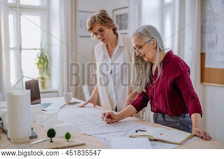 Mature Women Eco Architects With Model Of Modern Bulidings And Blueprints Working Together In Office
