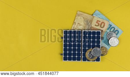 Photovoltaic Panel , Money And Plug Wire Isolated On Yellow Background. Olar Panel With Varied Value