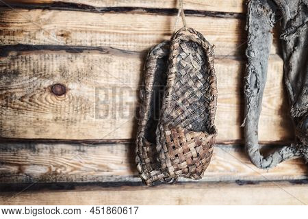 Old Bast Shoes On A Wooden Wall.