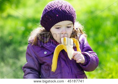 Pequena menina comer uma banana no Parque