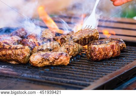 Preparing Meat Rolls Called Mici Or Mititei On Barbecue. Close Up Of Grill With Burning Fire With Fl
