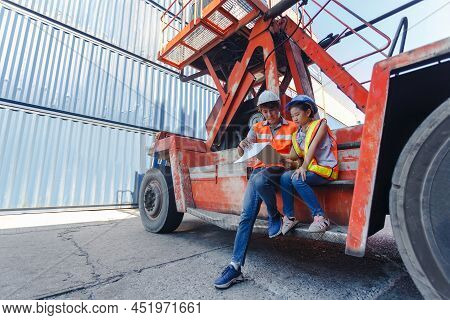 Man Engineering And Daughters Sitting On Forklift Working With Clipboard In Container Yard. Work Edu